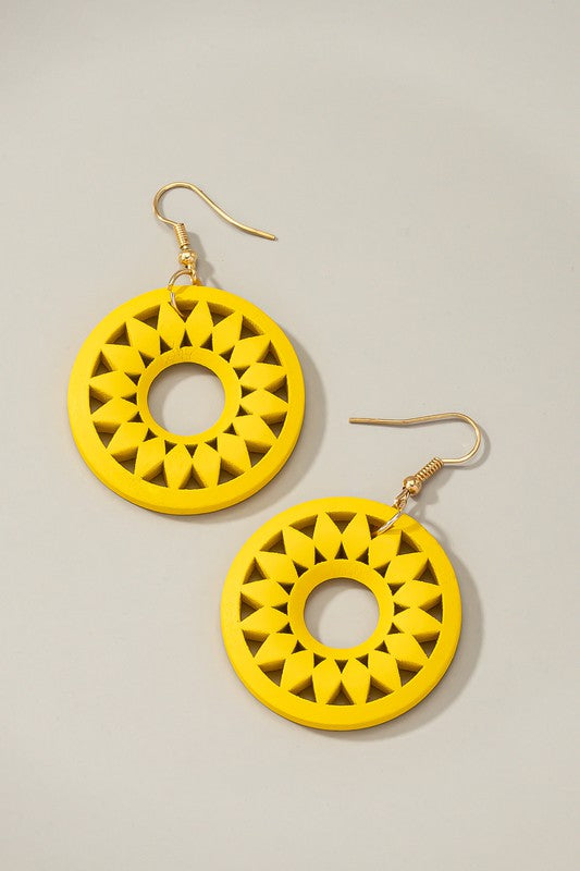 The NEW COLORS Cutout wood circle drop earrings, showcasing exquisite geometric patterns in black, brown, yellow, and orange, are elegantly arranged on a white surface.