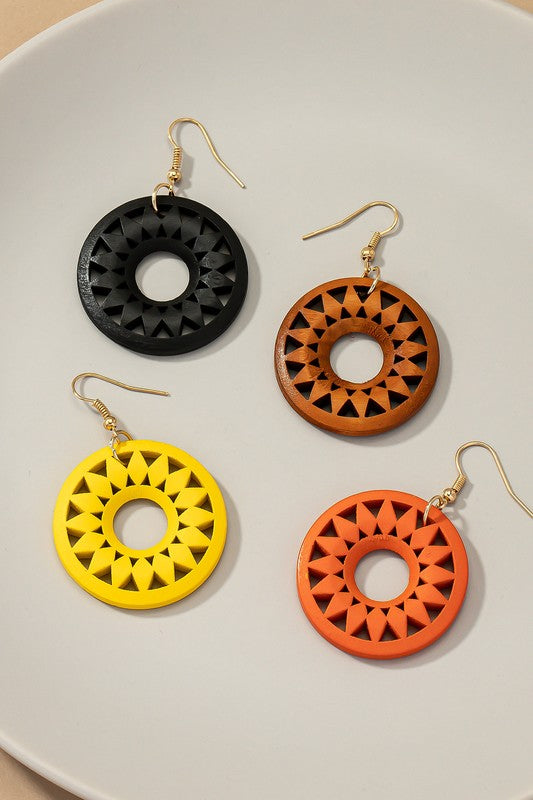 The NEW COLORS Cutout wood circle drop earrings, showcasing exquisite geometric patterns in black, brown, yellow, and orange, are elegantly arranged on a white surface.