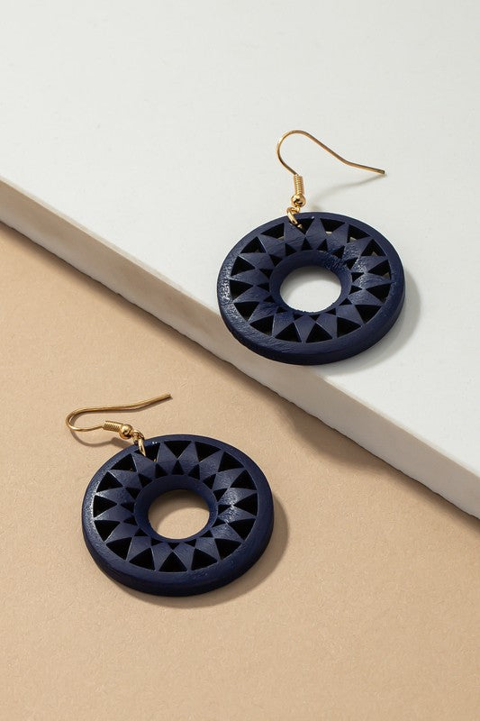 The NEW COLORS Cutout wood circle drop earrings, showcasing exquisite geometric patterns in black, brown, yellow, and orange, are elegantly arranged on a white surface.