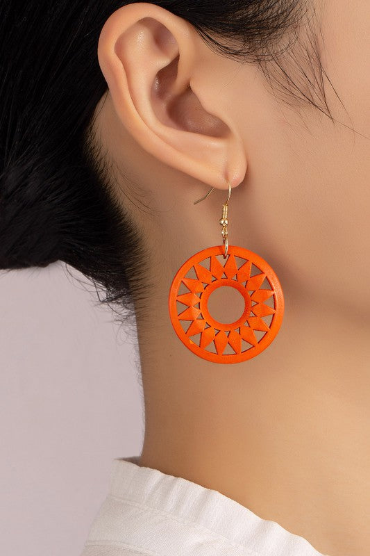 The NEW COLORS Cutout wood circle drop earrings, showcasing exquisite geometric patterns in black, brown, yellow, and orange, are elegantly arranged on a white surface.