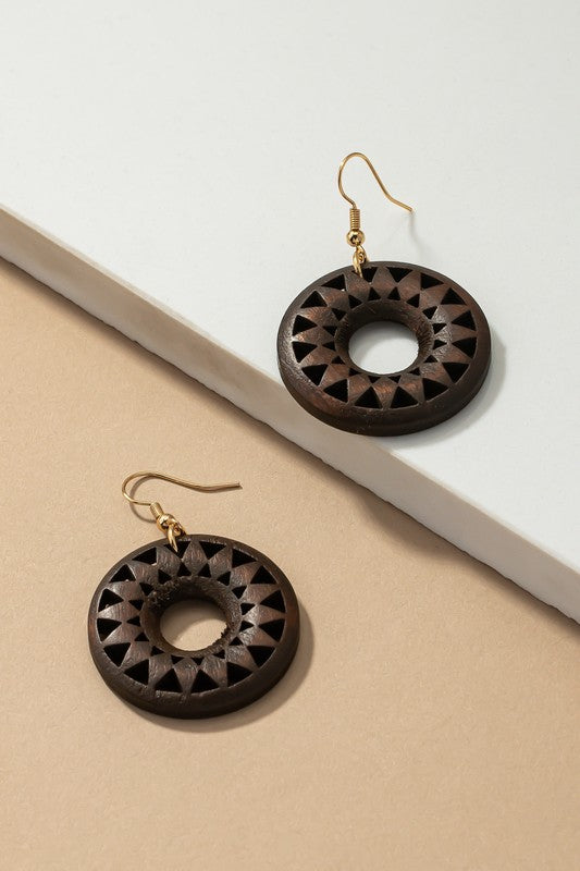 The NEW COLORS Cutout wood circle drop earrings, showcasing exquisite geometric patterns in black, brown, yellow, and orange, are elegantly arranged on a white surface.