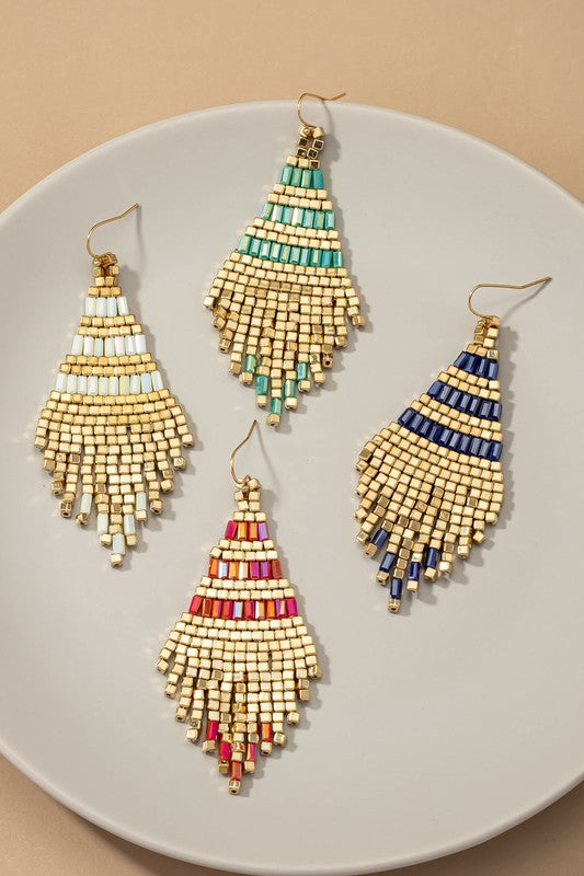 Four pairs of Handmade metallic cube bead tassel earrings, available in teal, navy, white, and multicolored shades, are elegantly arranged on a white plate.