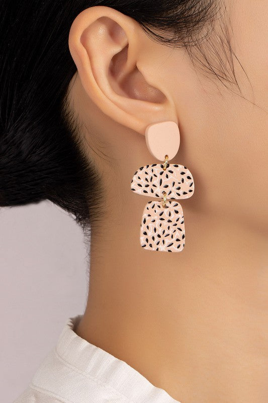 A pair of Flower Pattern Printed Acrylic Drop Earrings, featuring a lightweight pink design with geometric shapes and floral cutouts, displayed on a gray surface.