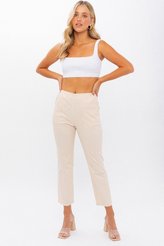 Person wearing High-Waisted Crop Pants in beige with a cropped length and clear high-heeled sandals stands against a white background. One hand is on their hip.