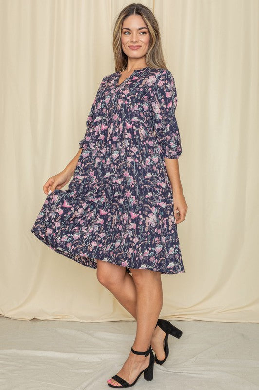 A woman in a Floral Notch Neck Midi Dress stands near a brick wall and window.