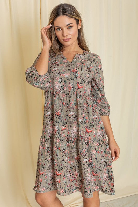 A person elegantly poses in front of a light curtain backdrop, wearing the Floral Notch Neck Midi Dress, crafted from 100% polyester and featuring three-quarter sleeves.