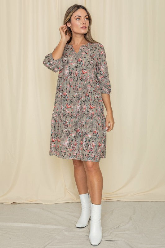 A person elegantly poses in front of a light curtain backdrop, wearing the Floral Notch Neck Midi Dress, crafted from 100% polyester and featuring three-quarter sleeves.