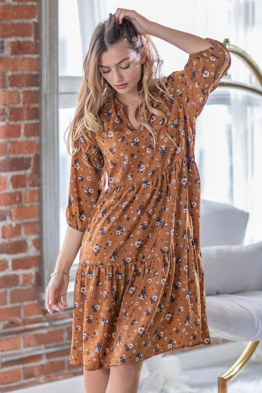 A person elegantly poses in front of a light curtain backdrop, wearing the Floral Notch Neck Midi Dress, crafted from 100% polyester and featuring three-quarter sleeves.