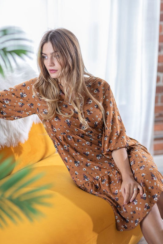 A person elegantly poses in front of a light curtain backdrop, wearing the Floral Notch Neck Midi Dress, crafted from 100% polyester and featuring three-quarter sleeves.