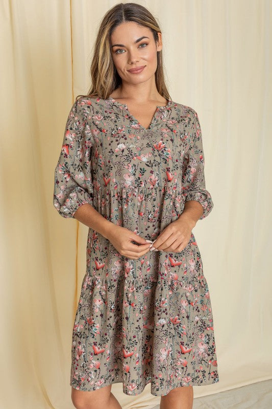 A person elegantly poses in front of a light curtain backdrop, wearing the Floral Notch Neck Midi Dress, crafted from 100% polyester and featuring three-quarter sleeves.