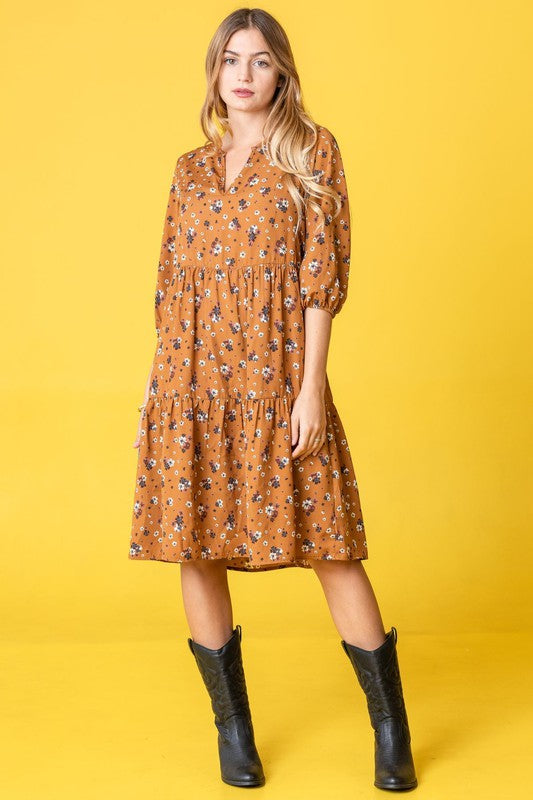 A person elegantly poses in front of a light curtain backdrop, wearing the Floral Notch Neck Midi Dress, crafted from 100% polyester and featuring three-quarter sleeves.