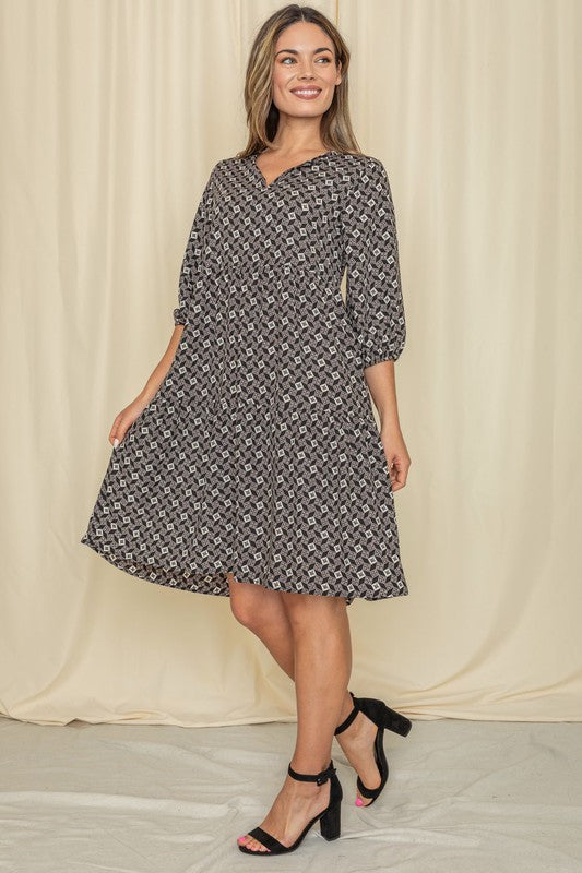 A person stands posing in the Square Print Notch Neck Midi Dress, showcasing its square print and three-quarter sleeves, against a plain backdrop.