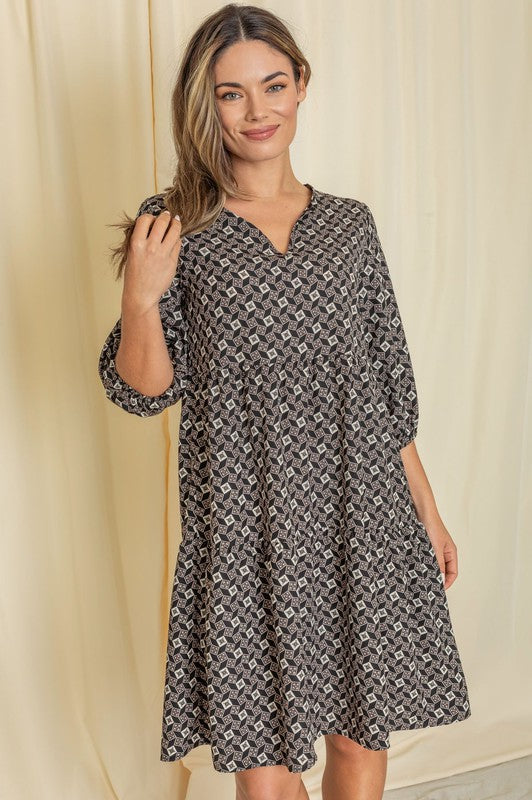 A woman wearing a Plus Square Print Notch Neck Midi Dress paired with black heels stands in front of a beige backdrop.