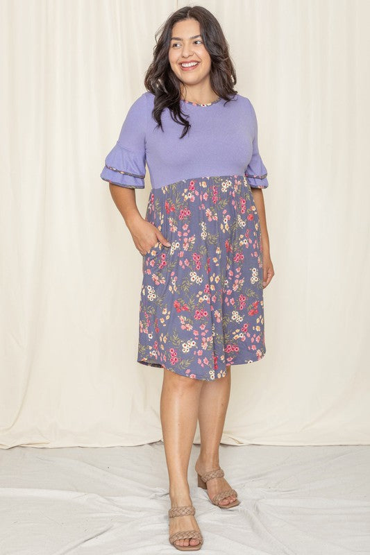 A woman stands wearing the Double Ruffle Sleeve Midi Dress, featuring a knee-length style with a white top and floral skirt made from polyester spandex, set against a beige curtain background.