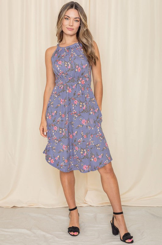 A woman stands gracefully against a light-colored background, modeling the Floral Halter Top Midi Dress, beautifully crafted in the United States.