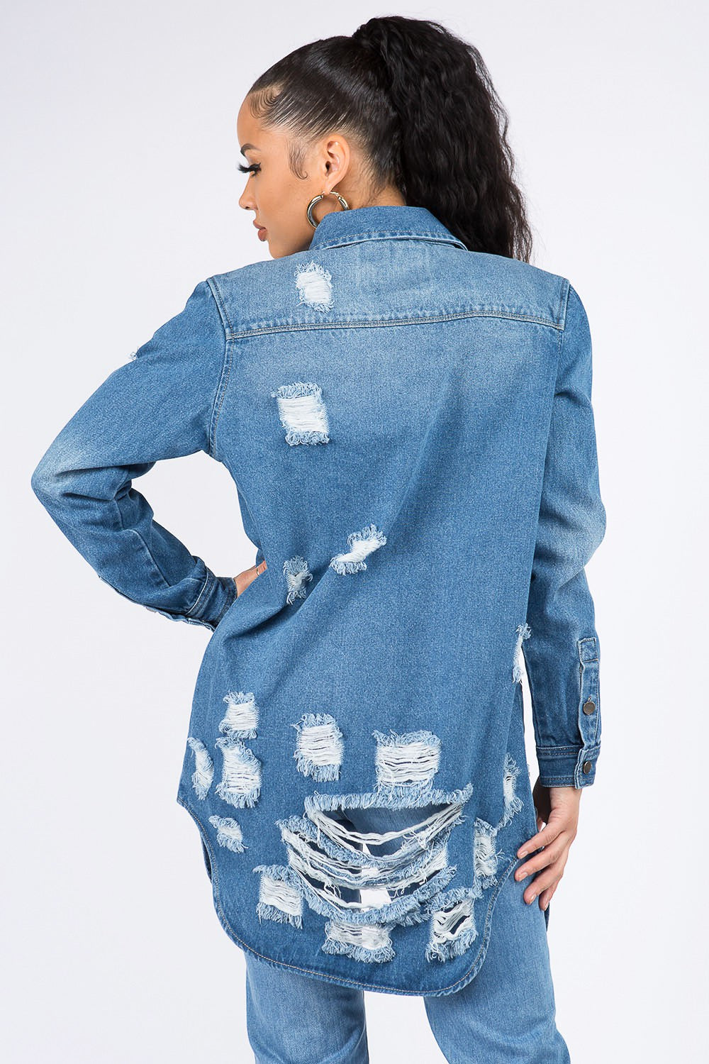 A woman wearing the American Bazi Distressed Button Down Denim Shirt Jacket and jeans paired with a white crop top exudes vintage-inspired charm as she poses with one hand on her head against a plain background.