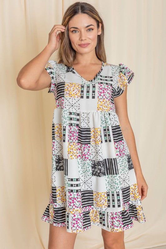 A woman wearing the Mix Print Flutter Sleeve Mini Dress, featuring a combination of floral and geometric patterns, smiles in front of a beige curtain, with the flutter sleeves adding an elegant touch.