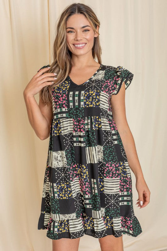 A woman wearing the Mix Print Flutter Sleeve Mini Dress, featuring a combination of floral and geometric patterns, smiles in front of a beige curtain, with the flutter sleeves adding an elegant touch.