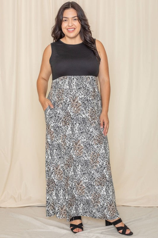 A woman is wearing the Plus Summer Sleeveless Maxi Dress, which features a mint green top paired with a skirt in a pink, blue, and brown tie-dye pattern. This American-made maxi dress, with its sleeveless design, stands out against the neutral background.