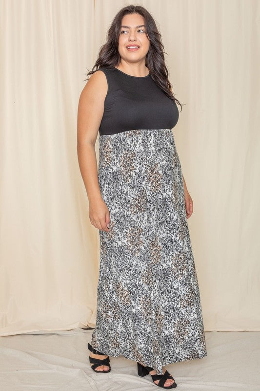 A woman is wearing the Plus Summer Sleeveless Maxi Dress, which features a mint green top paired with a skirt in a pink, blue, and brown tie-dye pattern. This American-made maxi dress, with its sleeveless design, stands out against the neutral background.