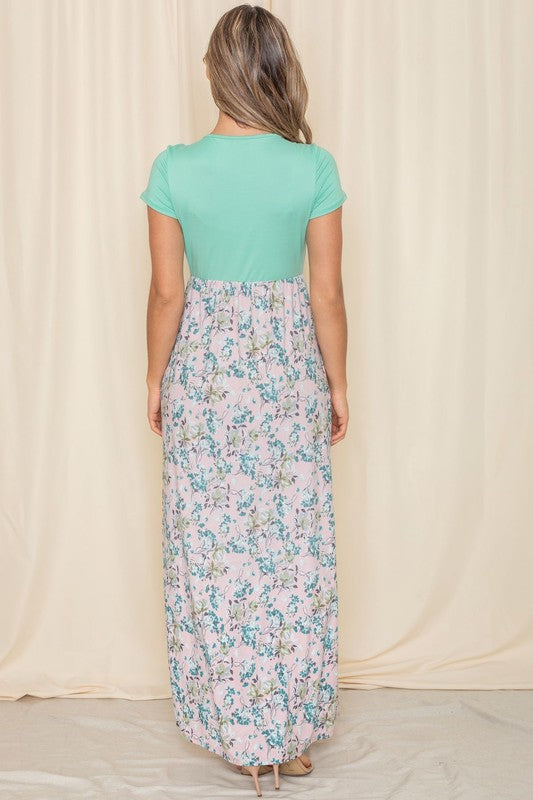 A woman in a short sleeve floral maxi dress, crafted from lightweight polyester spandex fabric, stands against a cream backdrop.