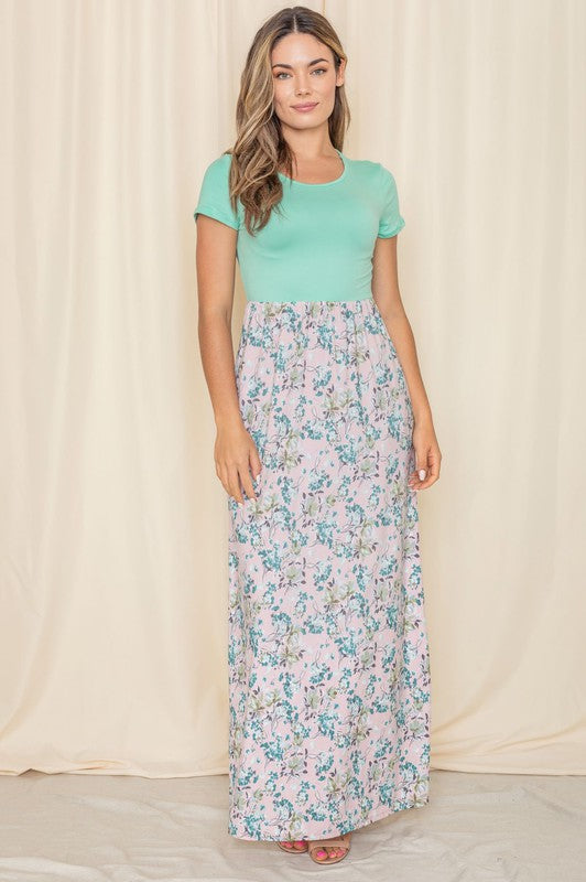 A woman in a short sleeve floral maxi dress, crafted from lightweight polyester spandex fabric, stands against a cream backdrop.