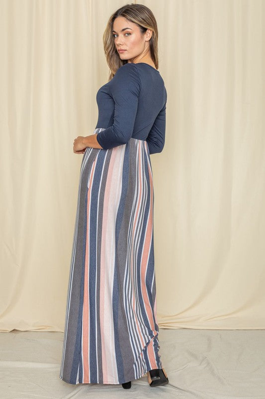 A woman wearing the Stripe Quarter Sleeve Maxi Dress, featuring navy blue quarter sleeves and multicolored vertical stripes, stands against a beige backdrop.