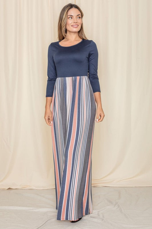 A woman wearing the Stripe Quarter Sleeve Maxi Dress, featuring navy blue quarter sleeves and multicolored vertical stripes, stands against a beige backdrop.