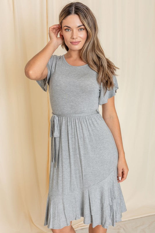 A person wearing a gray Ruffle Sash Midi Dress stands against a beige curtain backdrop.