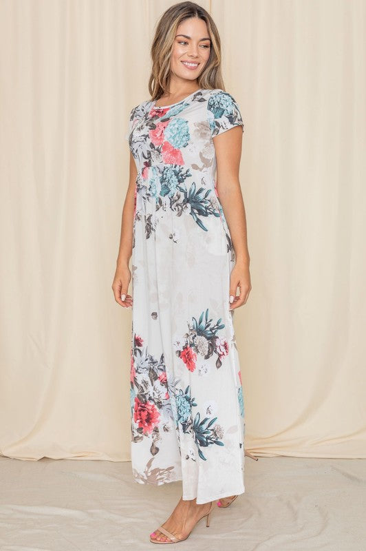 Against a beige backdrop, a woman elegantly showcases the Short Sleeve Floral Maxi Dress, designed and crafted in the United States.