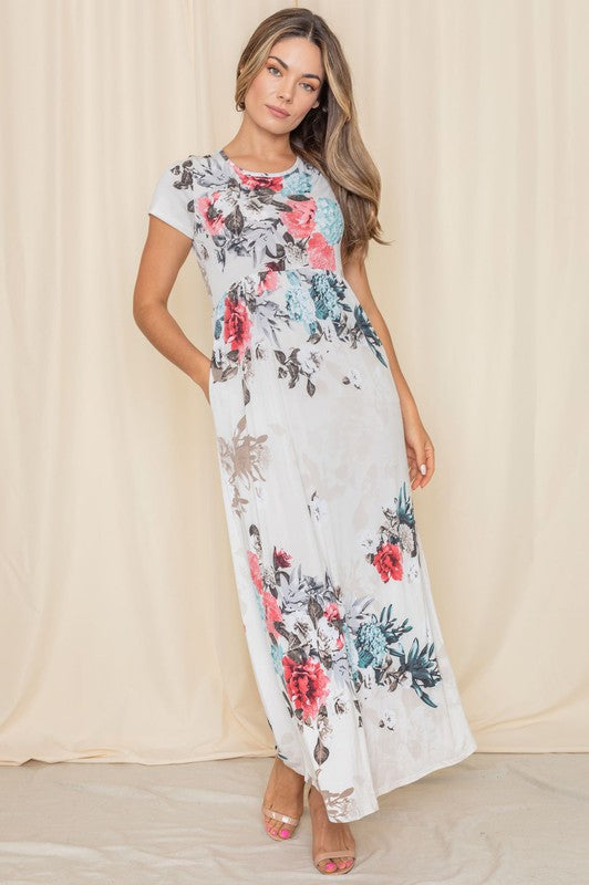 Against a beige backdrop, a woman elegantly showcases the Short Sleeve Floral Maxi Dress, designed and crafted in the United States.