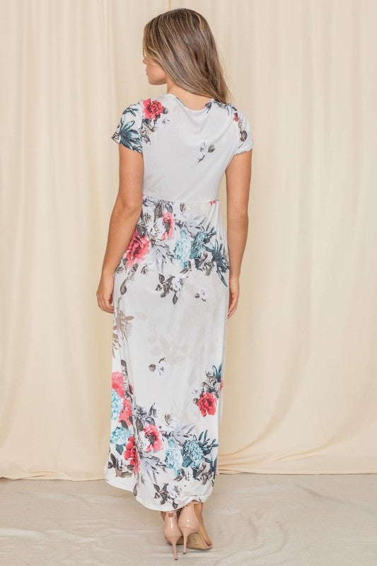 Against a beige backdrop, a woman elegantly showcases the Short Sleeve Floral Maxi Dress, designed and crafted in the United States.