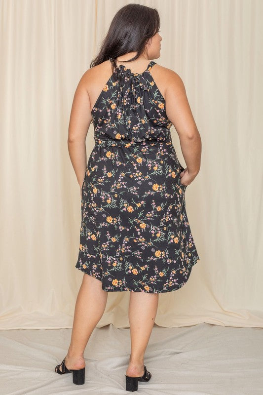 Wearing the elegant Plus Floral Halter Top Midi Dress, a person stands in front of a beige curtain, smiling with eyes closed. Crafted with care, this stunning piece is proudly made in the United States.