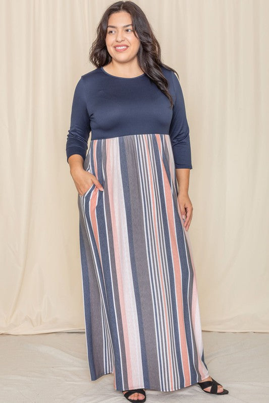 A person wearing the Plus Stripe Quarter Sleeve Maxi Dress, which showcases a navy top and a vertical striped skirt in blue, gray, and coral hues, stands in front of a beige curtain.