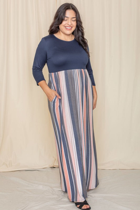 A person wearing the Plus Stripe Quarter Sleeve Maxi Dress, which showcases a navy top and a vertical striped skirt in blue, gray, and coral hues, stands in front of a beige curtain.