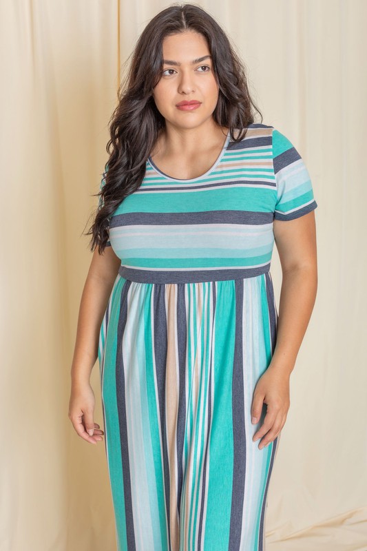 A person elegantly stands in front of a light-colored curtain, wearing the Plus Short Sleeve Stripe Maxi Dress in hues of blue, gray, and white.