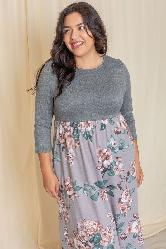 A person stands against a beige background wearing the Plus Quarter Sleeve Floral Maxi Dress, featuring a gray top with floral designs, proudly made in the United States.