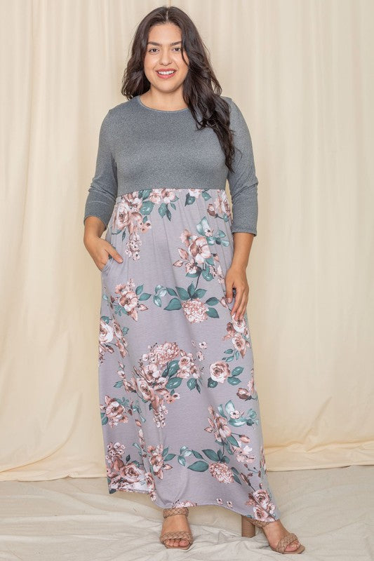 A person stands against a beige background wearing the Plus Quarter Sleeve Floral Maxi Dress, featuring a gray top with floral designs, proudly made in the United States.