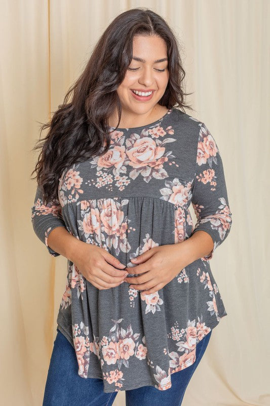 A woman in a Plus Floral Curved Hem Tunic and jeans smiles with her eyes closed, standing in front of a beige curtain.