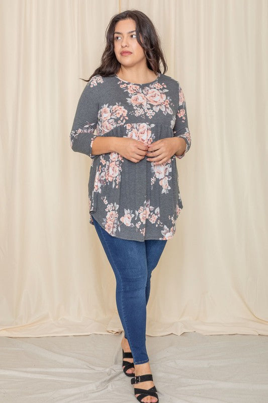 A woman in a Plus Floral Curved Hem Tunic and jeans smiles with her eyes closed, standing in front of a beige curtain.