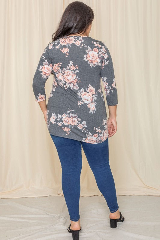 A woman in a Plus Floral Curved Hem Tunic and jeans smiles with her eyes closed, standing in front of a beige curtain.