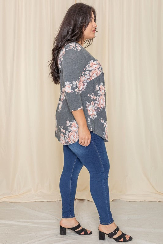 A woman in a Plus Floral Curved Hem Tunic and jeans smiles with her eyes closed, standing in front of a beige curtain.