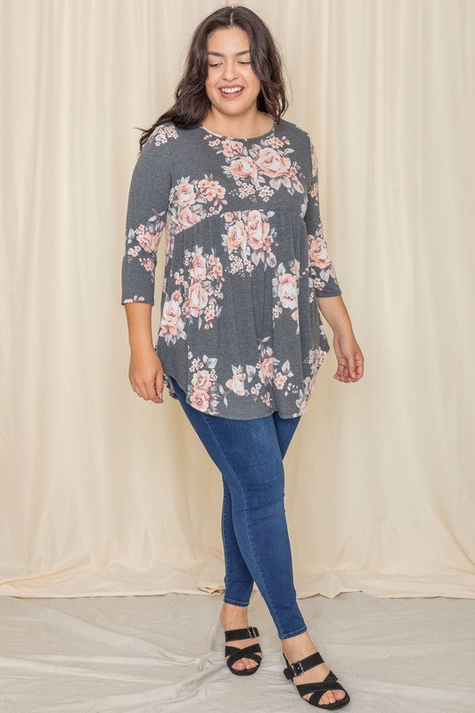 A woman in a Plus Floral Curved Hem Tunic and jeans smiles with her eyes closed, standing in front of a beige curtain.