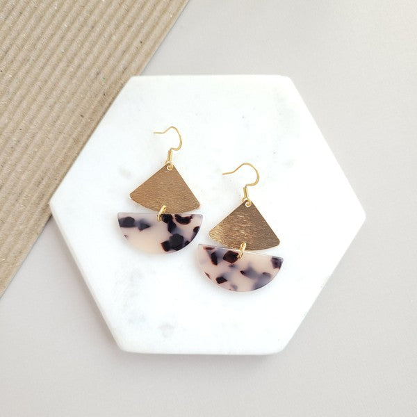 The Ava Blonde Tortoise earrings showcase geometric designs in blonde tortoise with gold-plated hooks, tastefully arranged on a marble hexagonal tray.