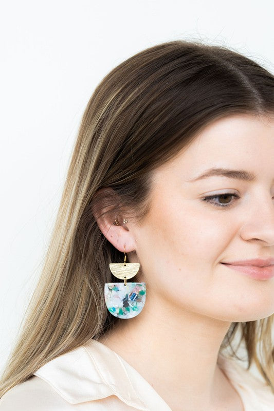 The Harper Spring Fling earrings boast colorful resin and gold-plated hooks, highlighting geometric elegance against a hexagonal white marble background. Crafted from plant-based acetate acrylic, these earrings offer a stylish and eco-friendly option.