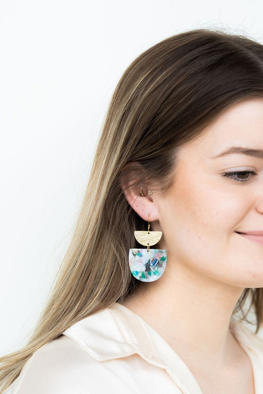 The Harper Spring Fling earrings boast colorful resin and gold-plated hooks, highlighting geometric elegance against a hexagonal white marble background. Crafted from plant-based acetate acrylic, these earrings offer a stylish and eco-friendly option.