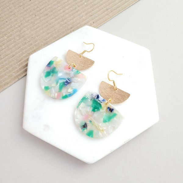 The Harper Spring Fling earrings boast colorful resin and gold-plated hooks, highlighting geometric elegance against a hexagonal white marble background. Crafted from plant-based acetate acrylic, these earrings offer a stylish and eco-friendly option.