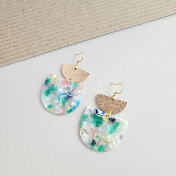 The Harper Spring Fling earrings boast colorful resin and gold-plated hooks, highlighting geometric elegance against a hexagonal white marble background. Crafted from plant-based acetate acrylic, these earrings offer a stylish and eco-friendly option.