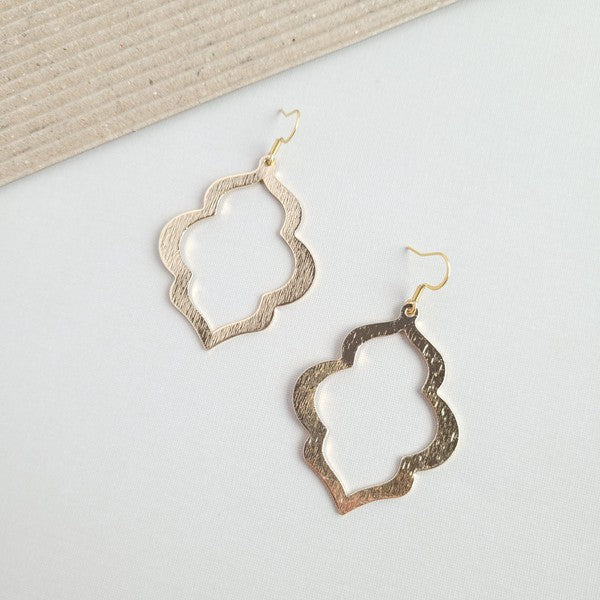 A person with long, wavy blonde hair is wearing the Talia Earrings in gold—a large geometric earring that serves as an elegant wardrobe staple, adding timeless charm to any look.