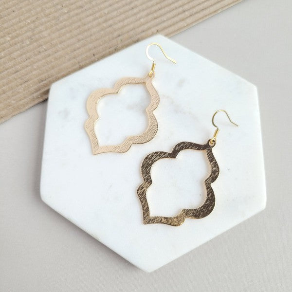 A person with long, wavy blonde hair is wearing the Talia Earrings in gold—a large geometric earring that serves as an elegant wardrobe staple, adding timeless charm to any look.